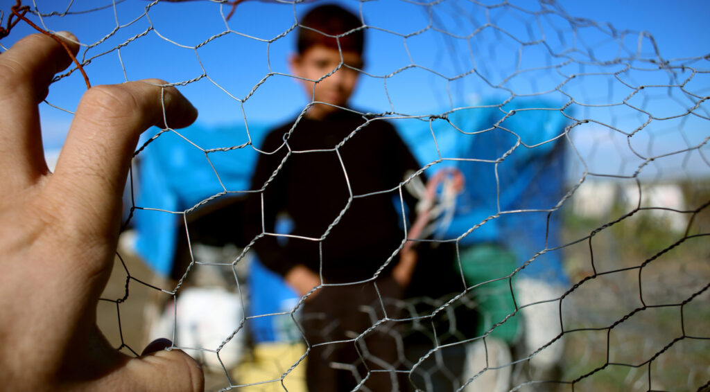 Refugee kid stands behind a wire fence