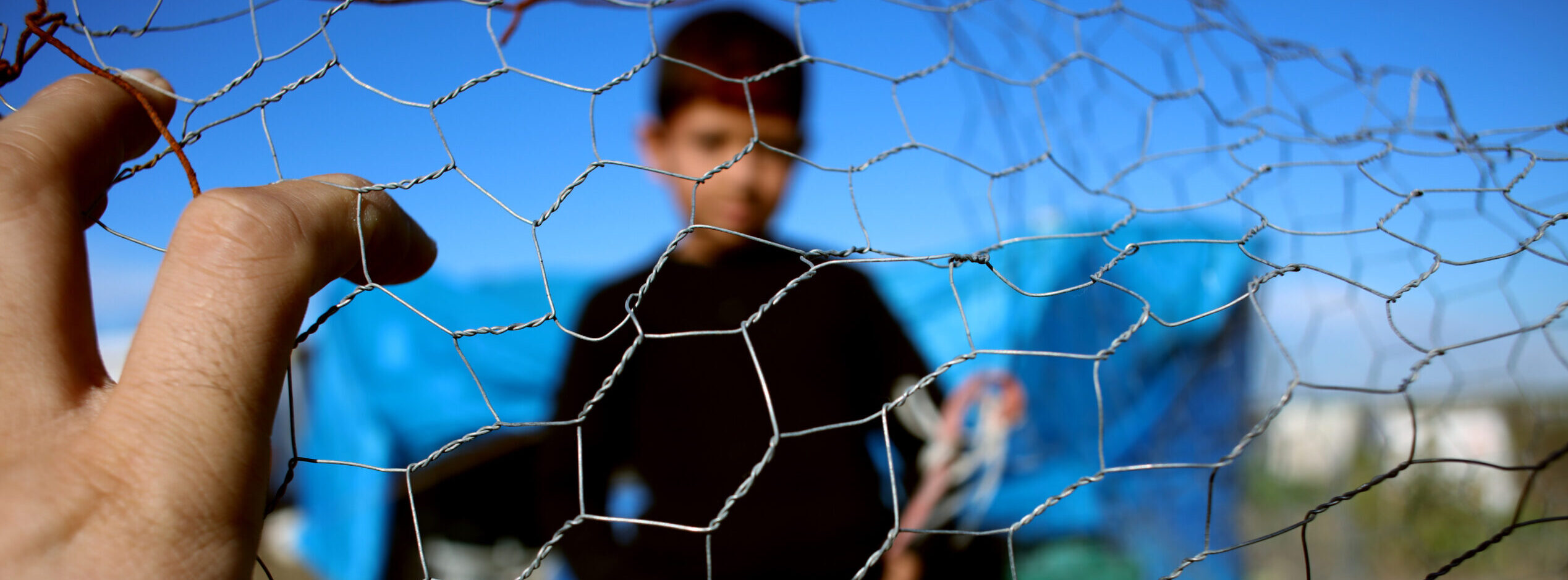 Refugee kid stands behind a wire fence